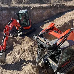 A backhoe excavator and skid steer are working on a deep excavation project