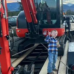 The son of KW & Sons is standing on a trailer in front of an excavator